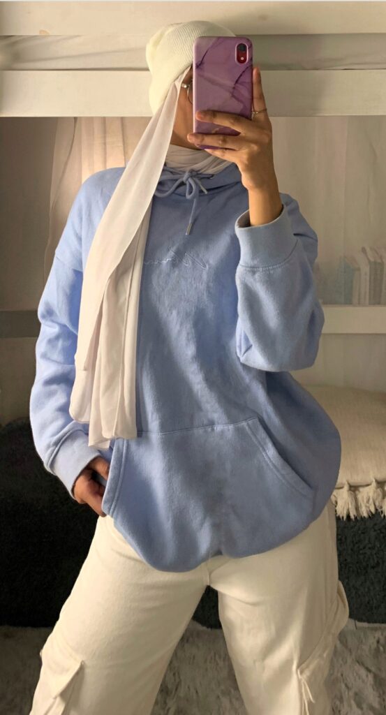 A hijabi wearing white beanie, baby blue hoodie, white cargo jeans and white hijab